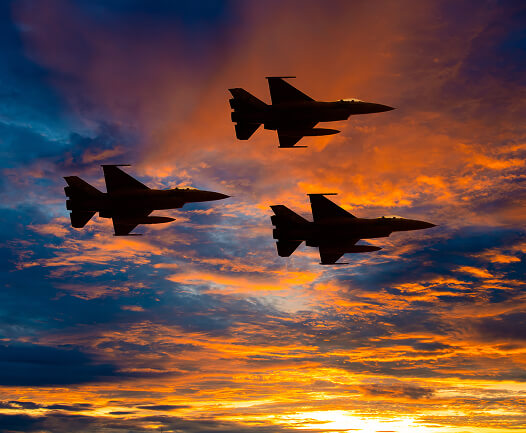 military-planes Silhouetted front view of a large military cargo aircraft on a runway during sunset, with its wings and engines casting shadows.
